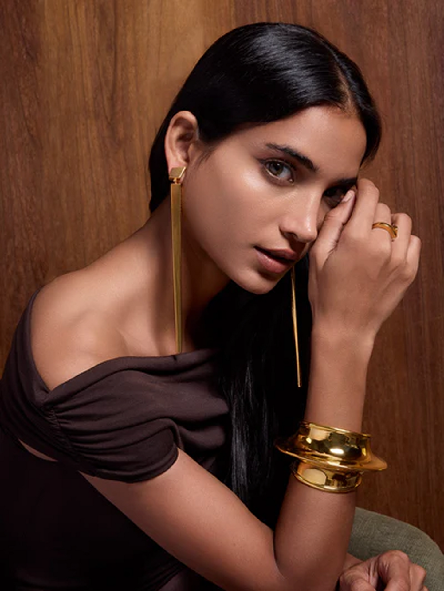 Woman wearing gold earrings and bracelet against a wooden background