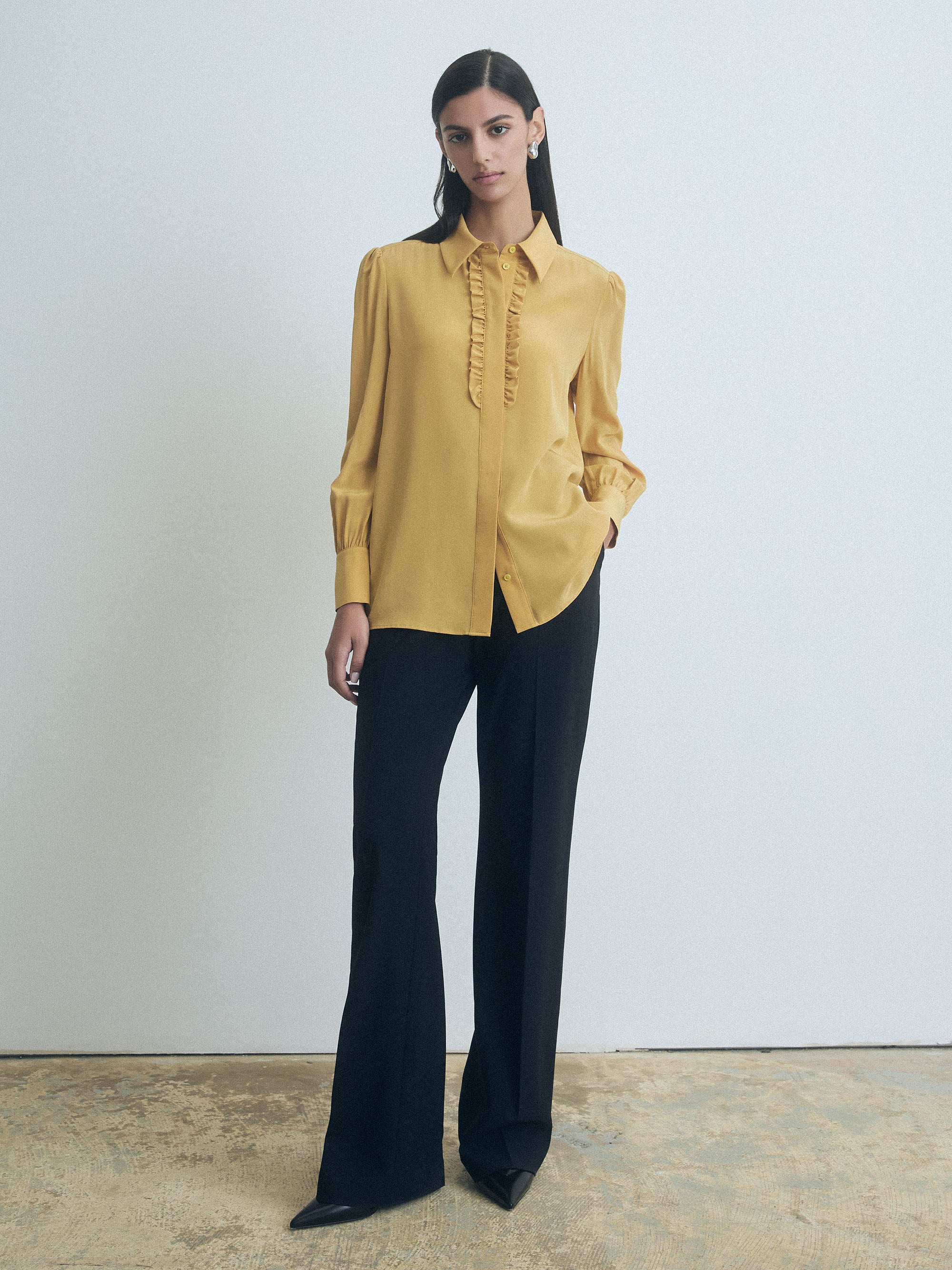 Woman wearing a judith and charles mustard yellow blouse and black pants against a plain background
