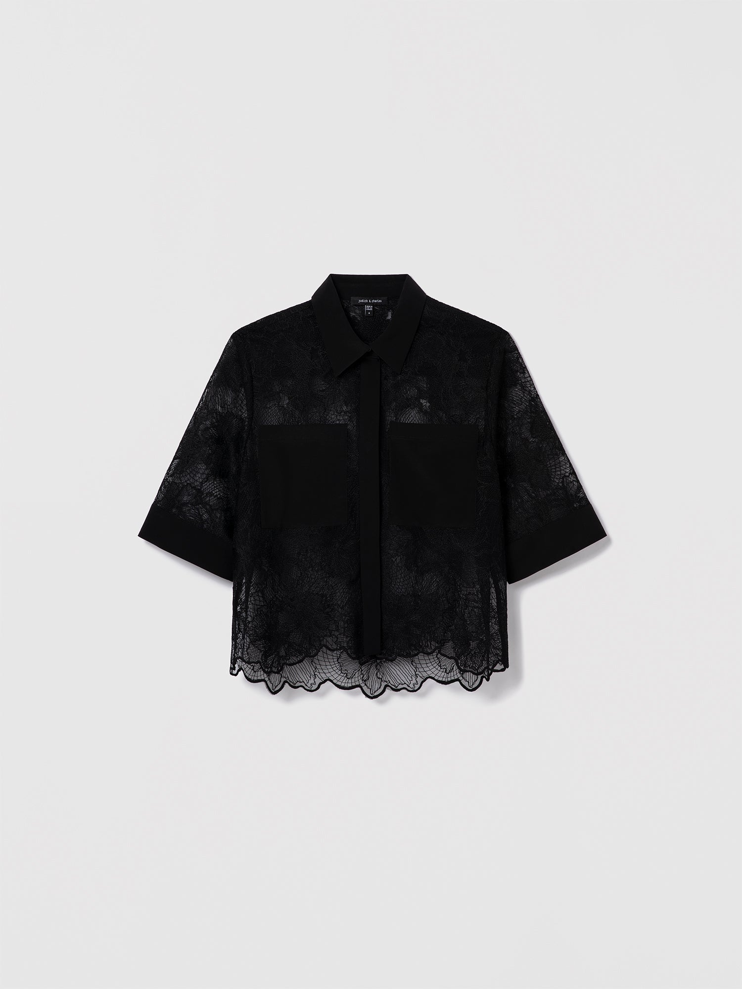 Black lace shirt by Judith & Charles featuring a stand collar, front button closure, two patch pockets, and scalloped lace hem; unlined.
