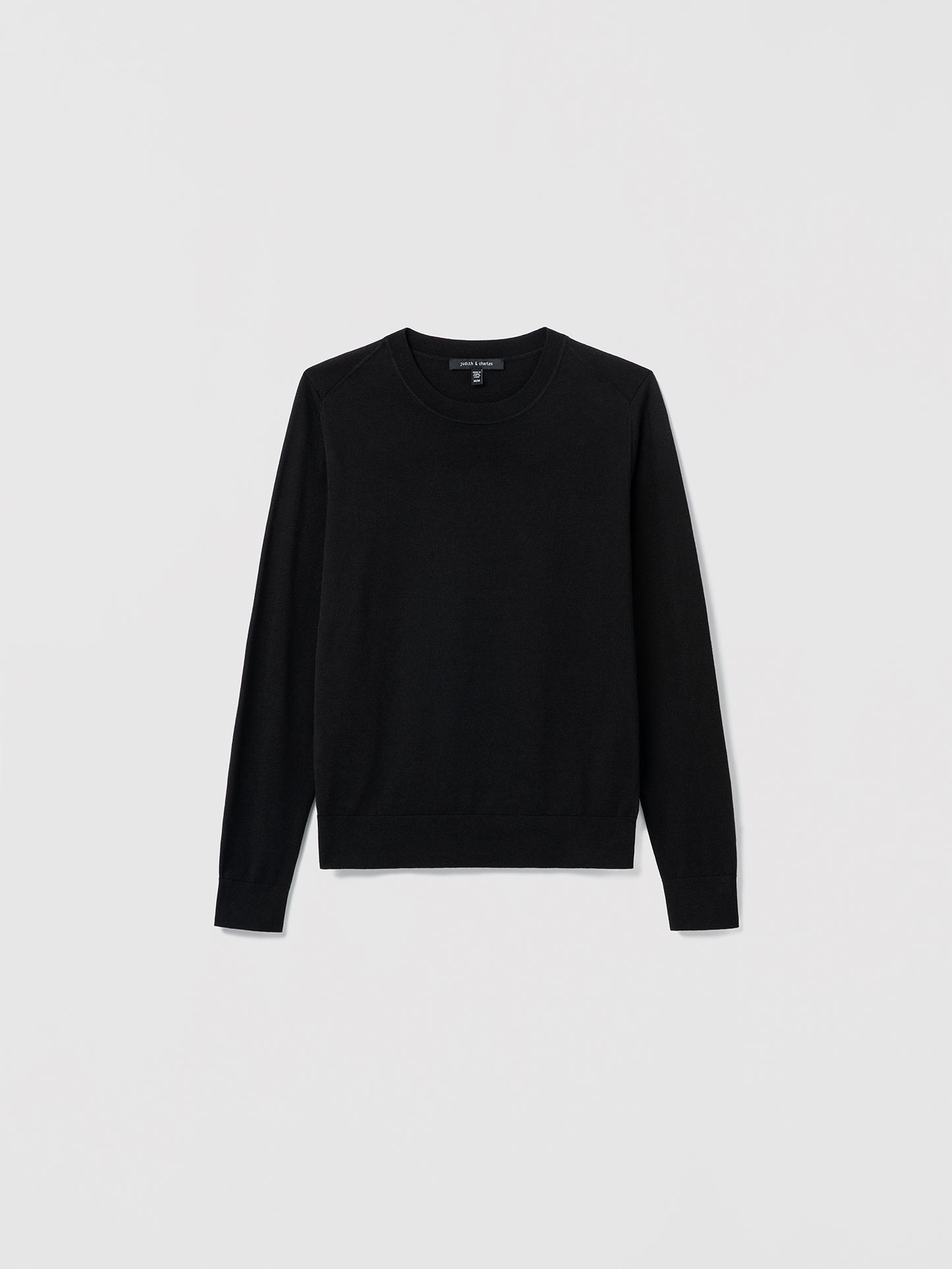 Flat‑lay of a black silk‑cotton crewneck sweater with long sleeves and refined ribbed trims.