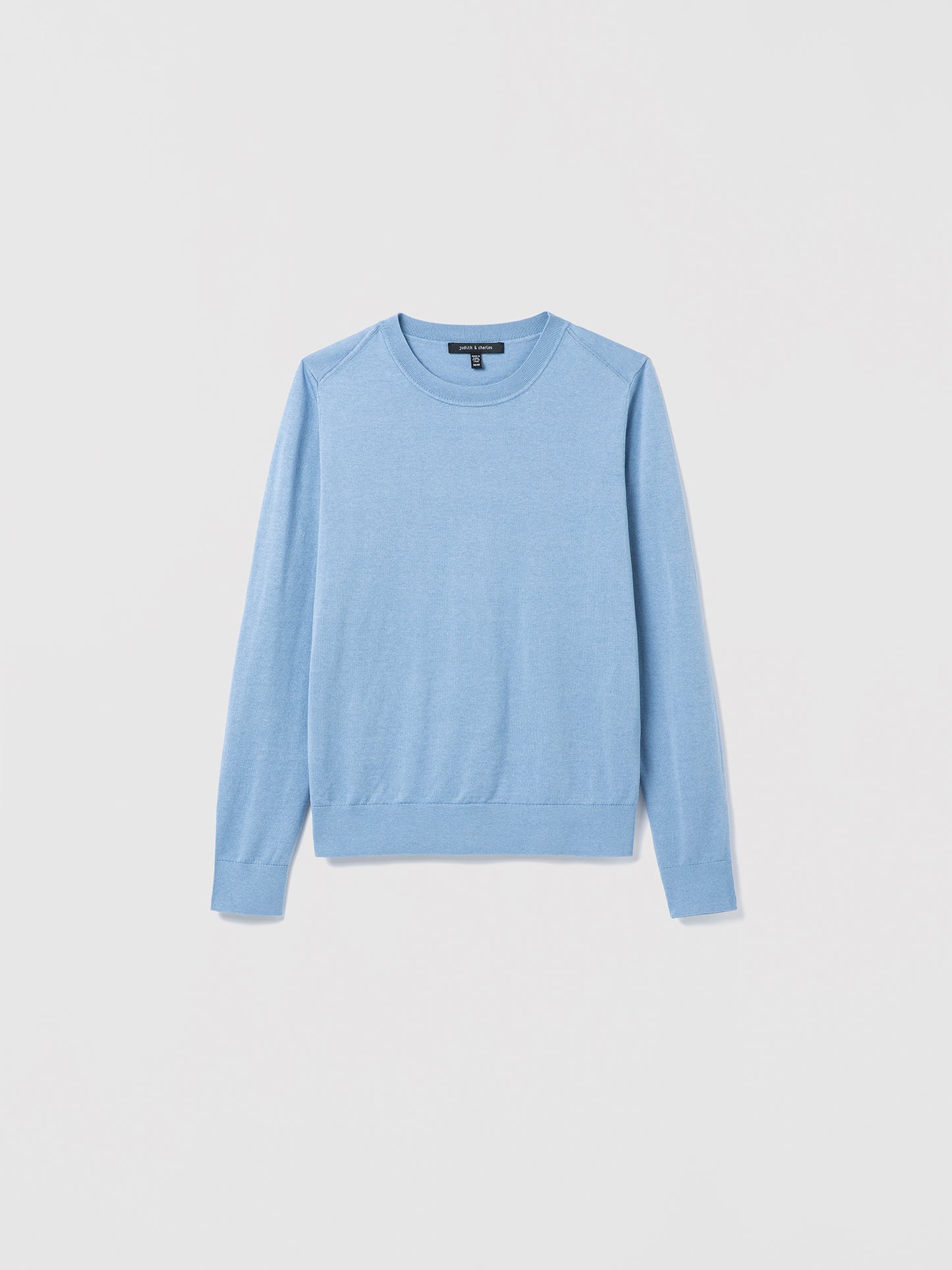 Flat‑lay of a smokey blue silk‑cotton crewneck sweater with long sleeves and refined ribbed trims.