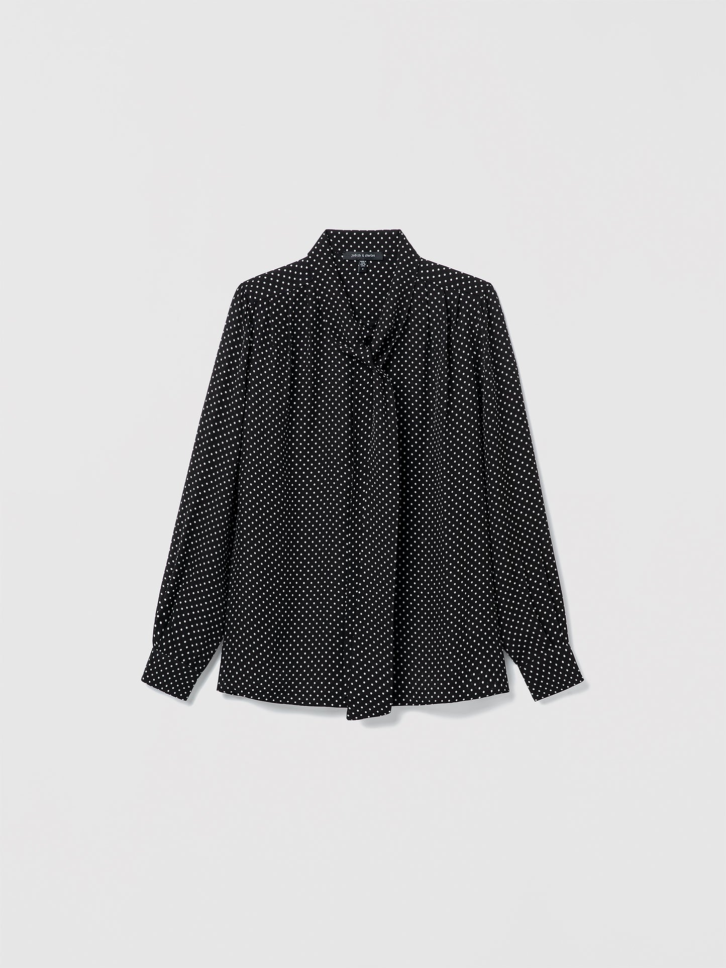 Flat lay of black and white silk blouse with long sleeves, pleats, and neck tie. Straight fit, unlined, with button closure 