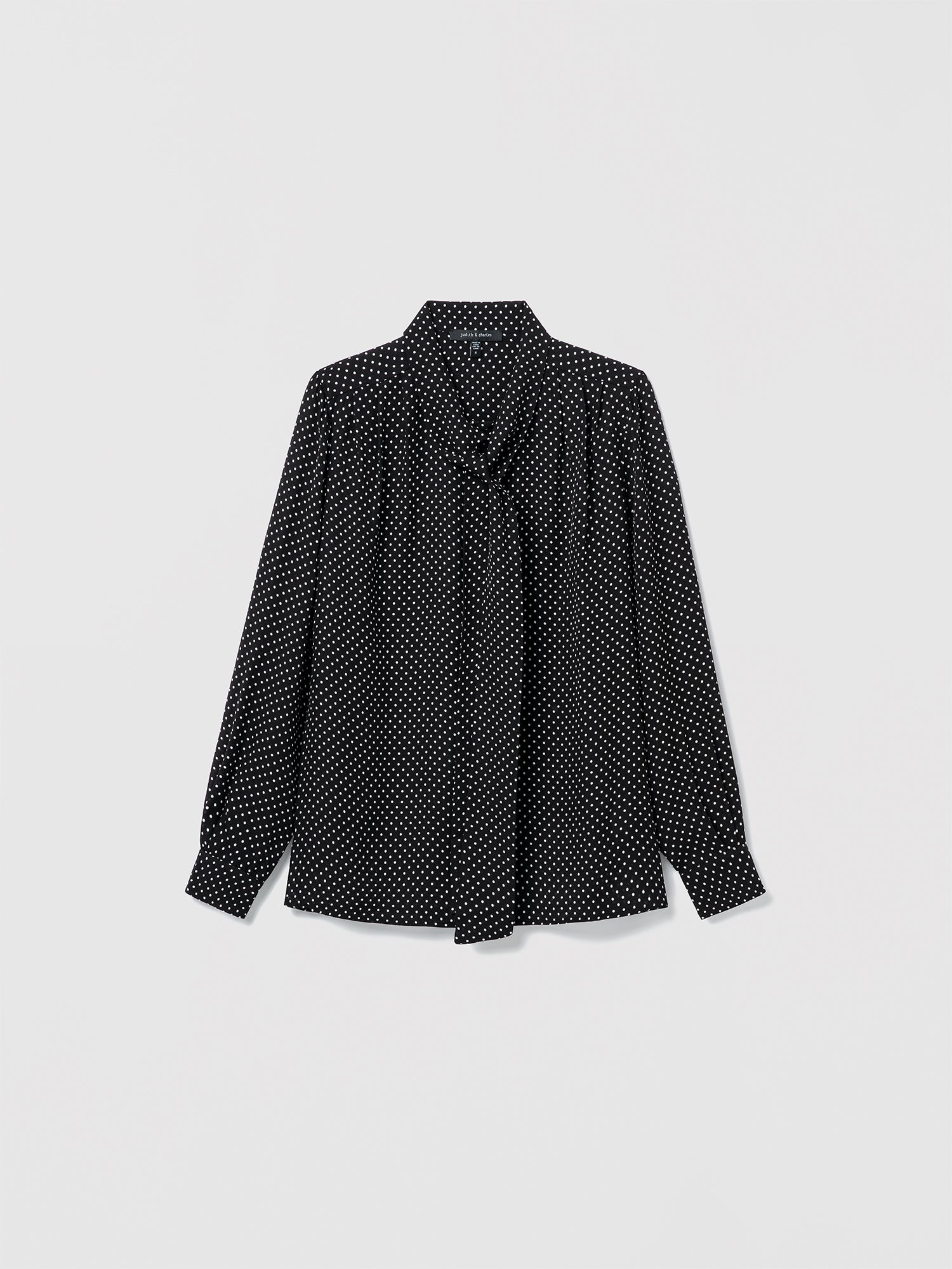 Flat lay of black and white silk blouse with long sleeves, pleats, and neck tie. Straight fit, unlined, with button closure 
